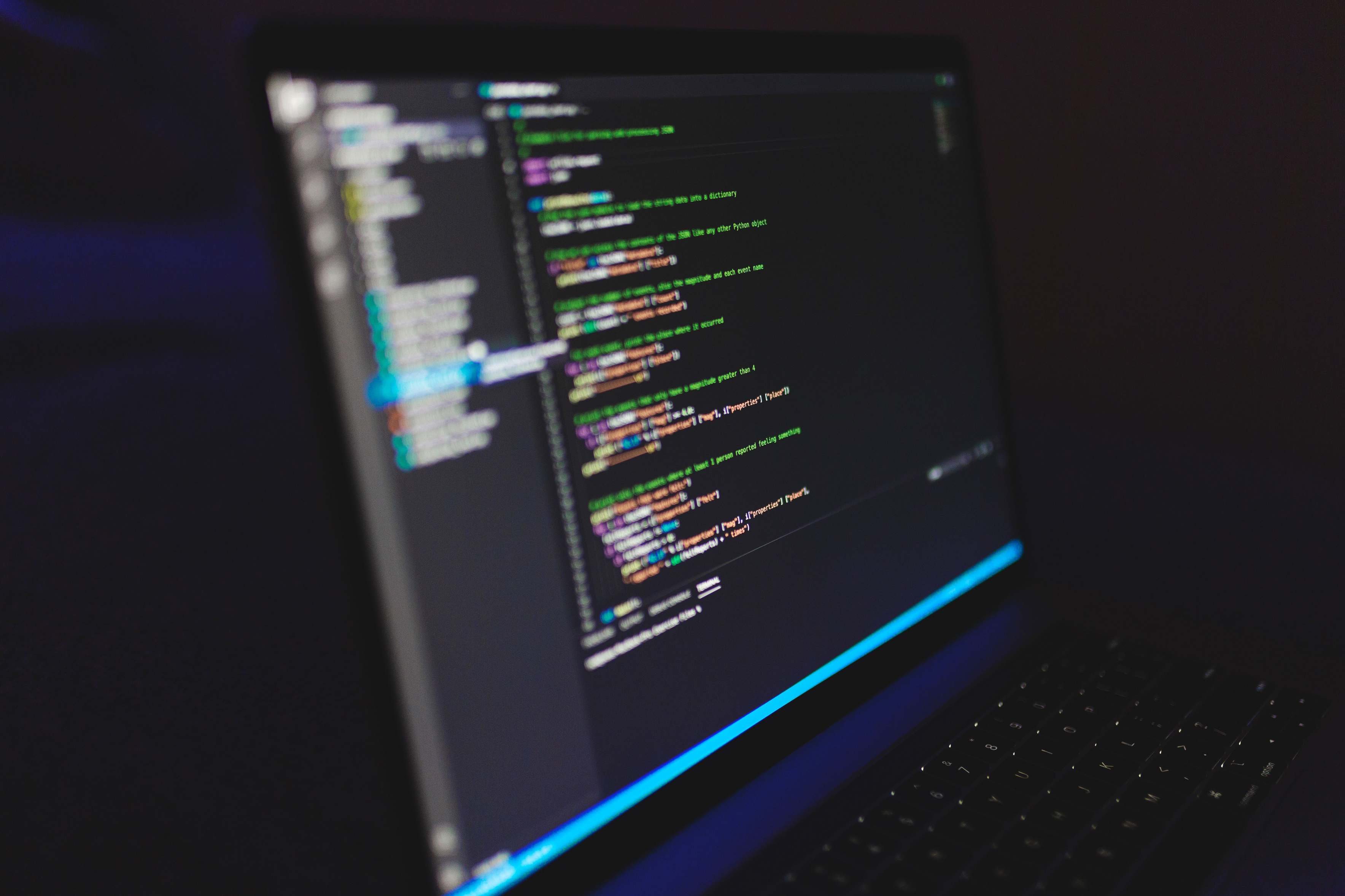 Laptop showing source code on a desk in a dark setting